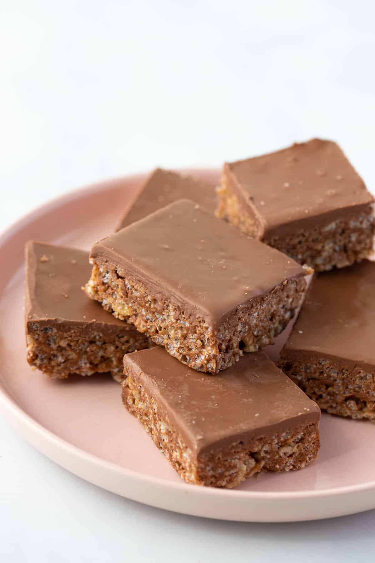 pieces of mars bar slice topped with chocolate, arranged on a pink plate.