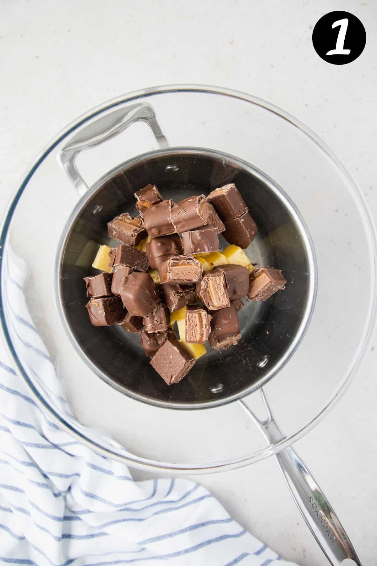 pieces of mars bar and cubes of butter in a glass bowl over a saucepan.