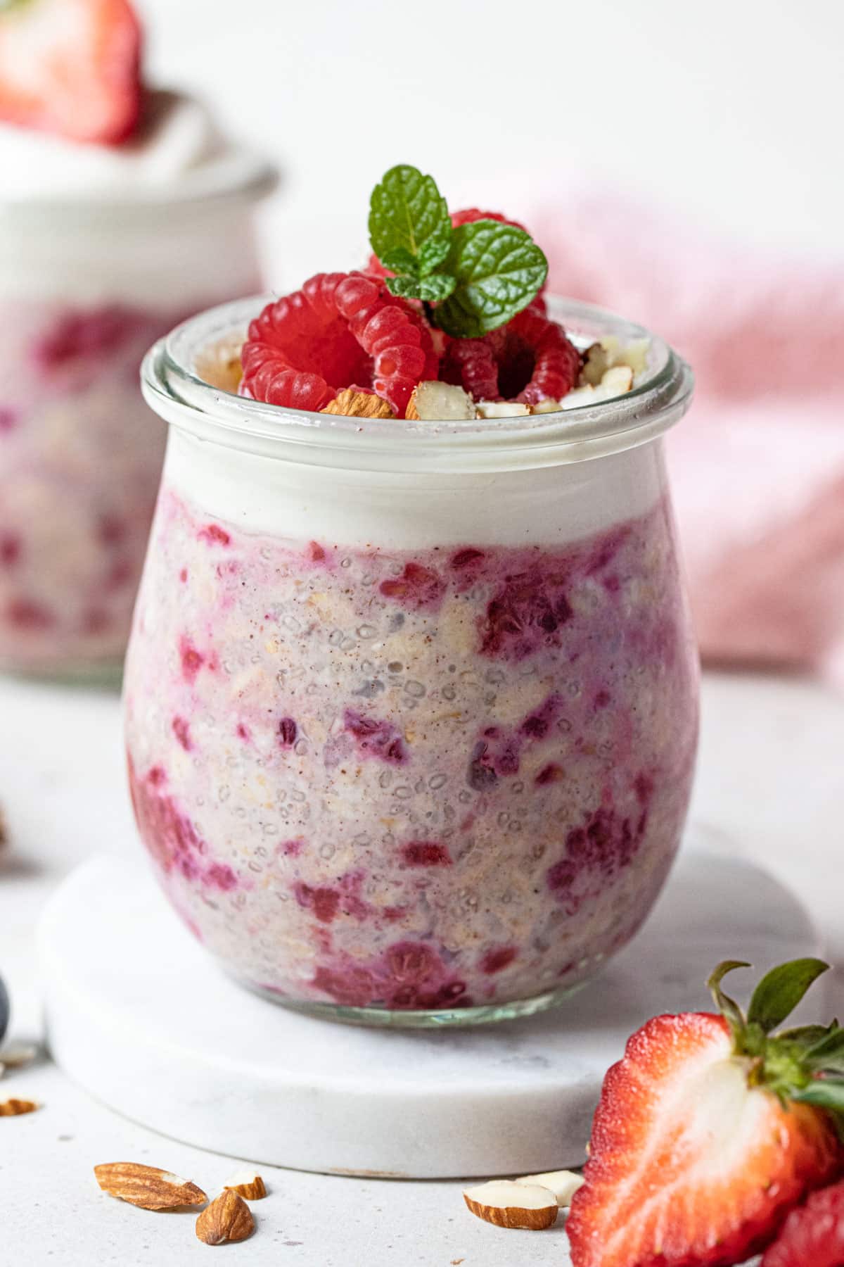 a jar of overnight oats filled with red raspberries and topped with fresh berries and yoghurt.