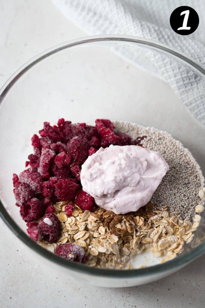 frozen raspberries, yoghurt and ingredients for overnight oats in a bowl.