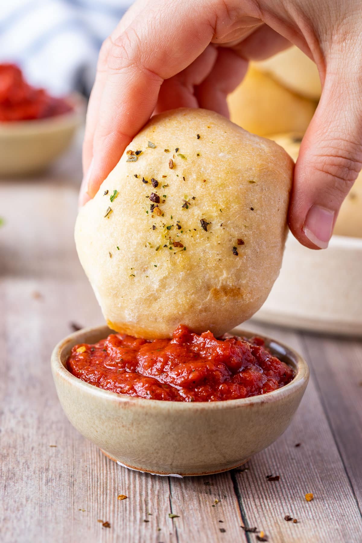 a hand dipping a pizza pocket into a bowl of pizza sauce.