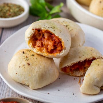 pizza rolls on a white plate, one is cut open to show the cheese and sauce filling.