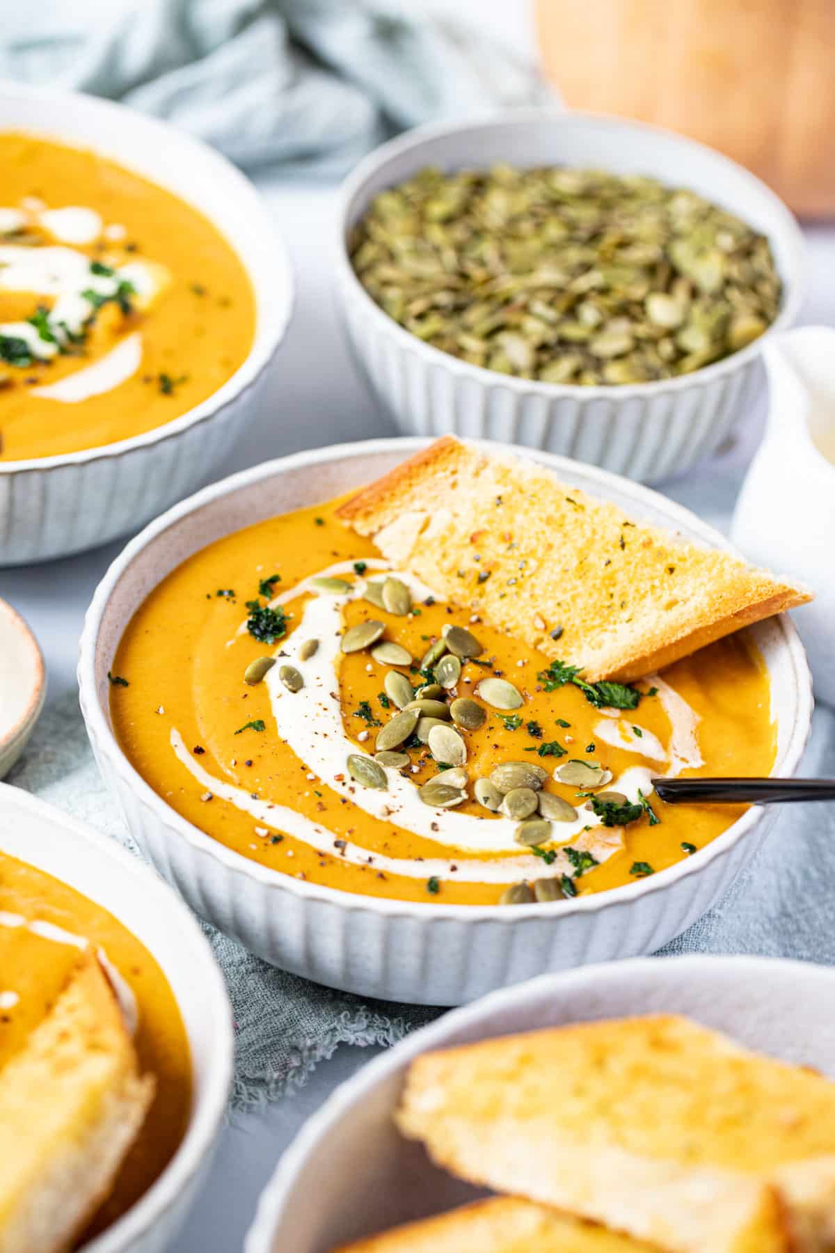 bowls of pumpkin soup on a table, topped with cream, pumpkin seeds and bread.