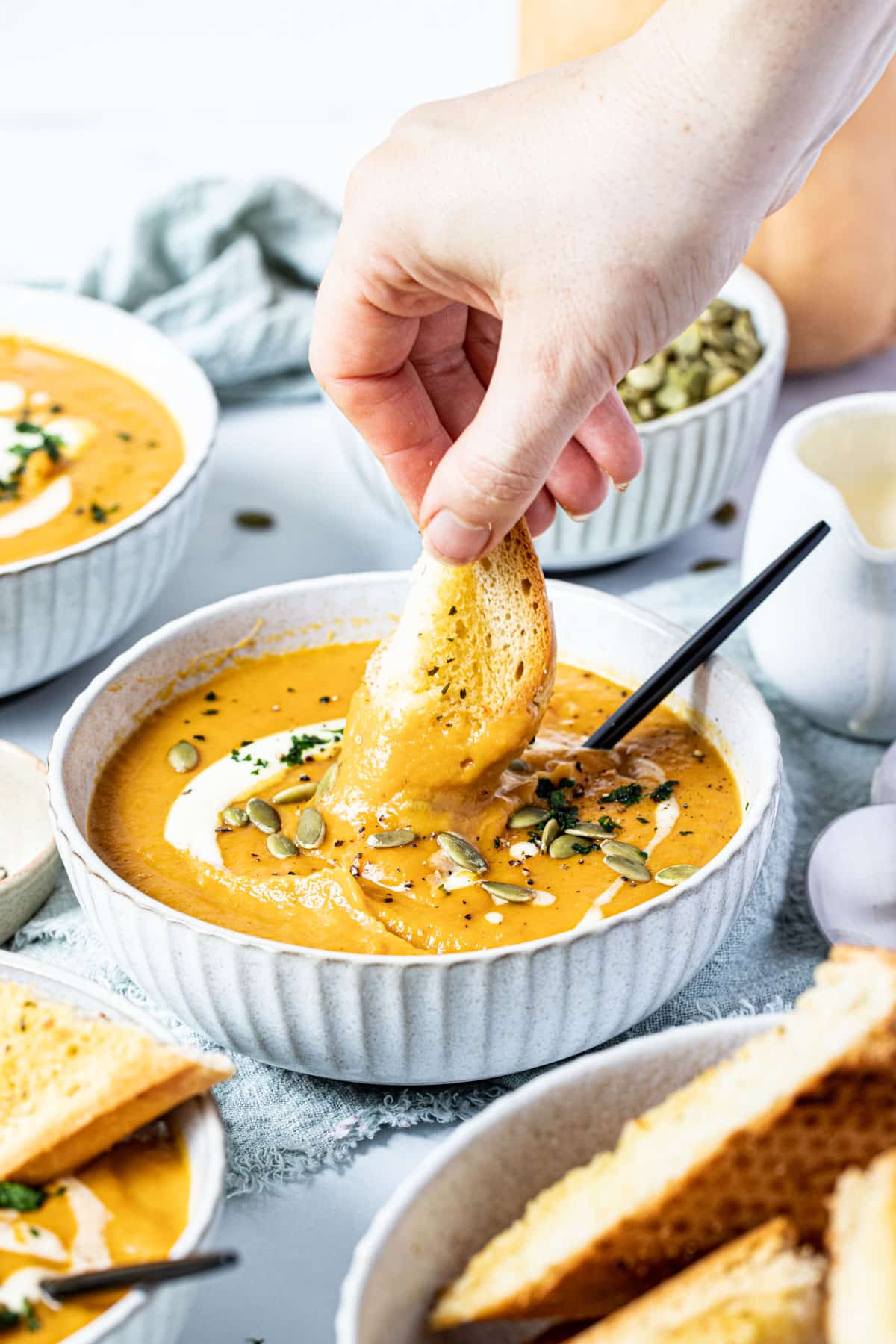 a hand dipping bread into a bowl of soup.