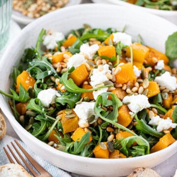 a bowl of roast pumpkin salad topped with pine nuts, rocket and goat cheese.