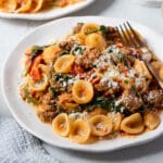 sausage pasta on a plate with cheese and a fork.