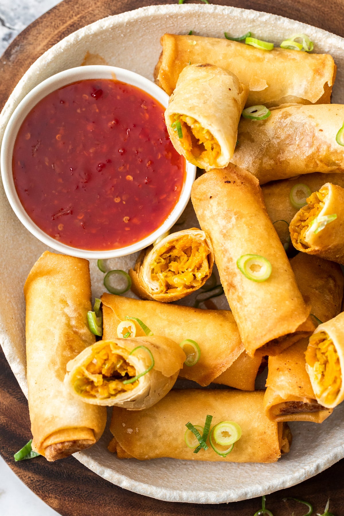 a plate of spring rolls with spring onion and sweet chilli sauce.