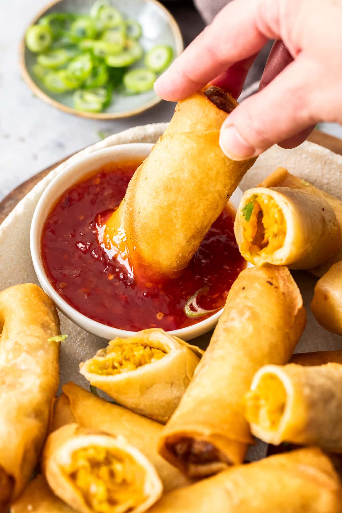 a hand dipping a spring roll into a dish of sweet chilli sauce.
