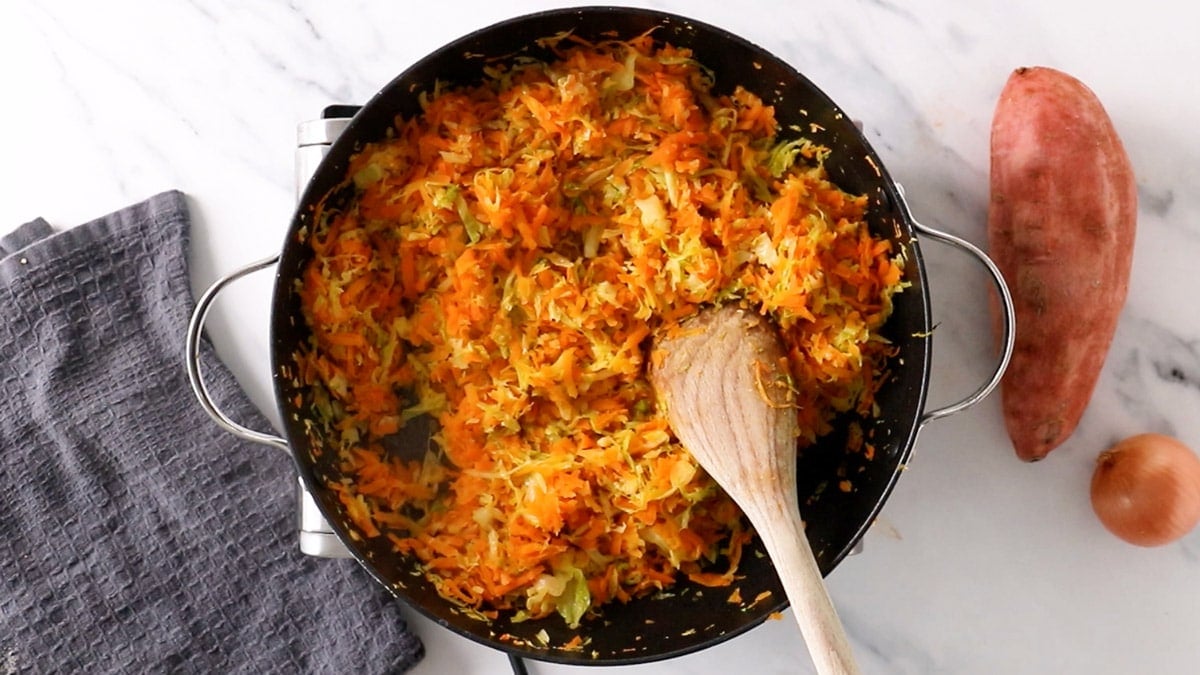 cooked, shredded vegetables in a frying pan with a wooden spoon.