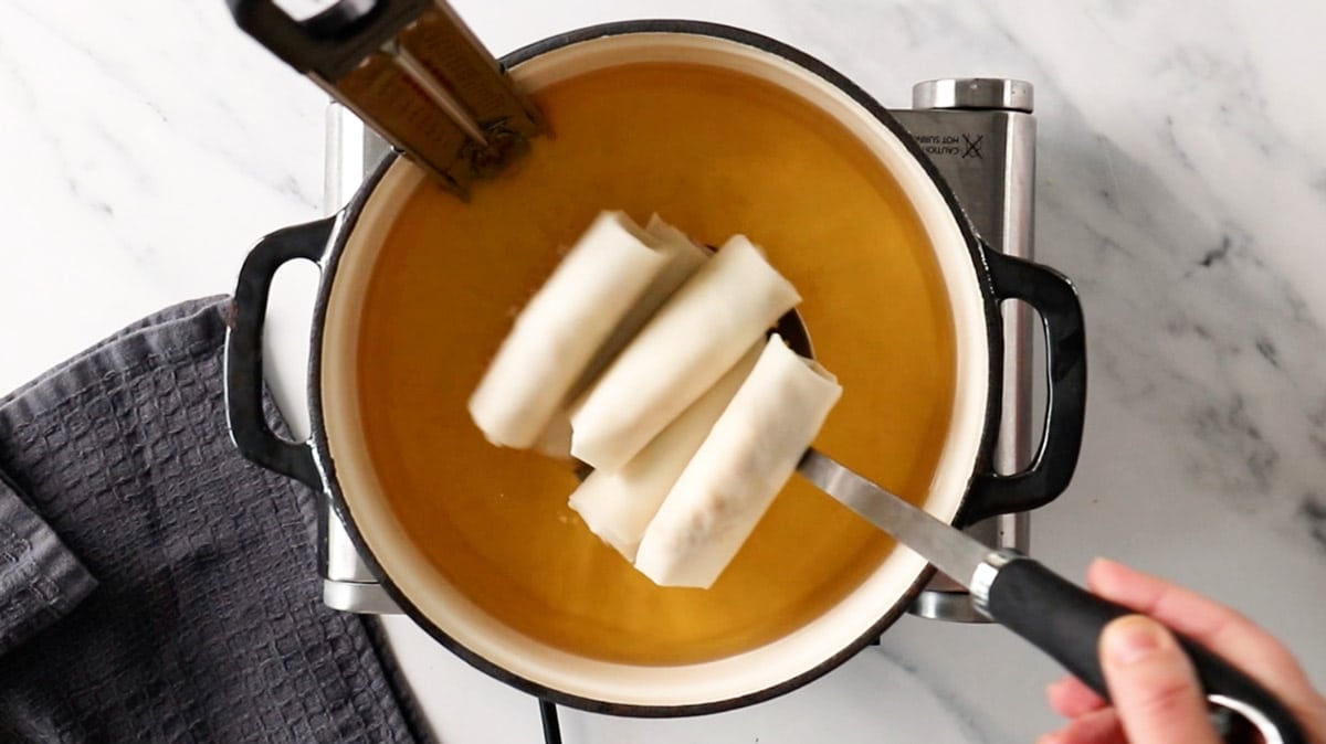 spring rolls being placed into a pan of oil.