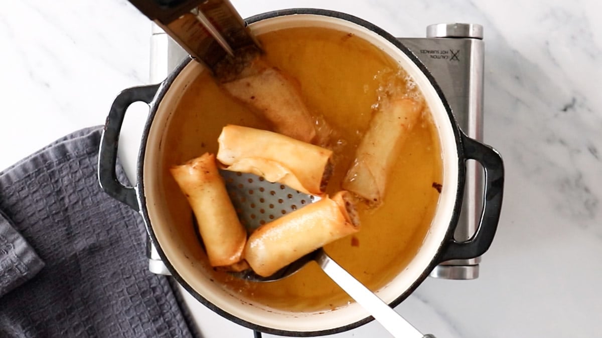 finished spring rolls bring removed from a pan filled with oil.