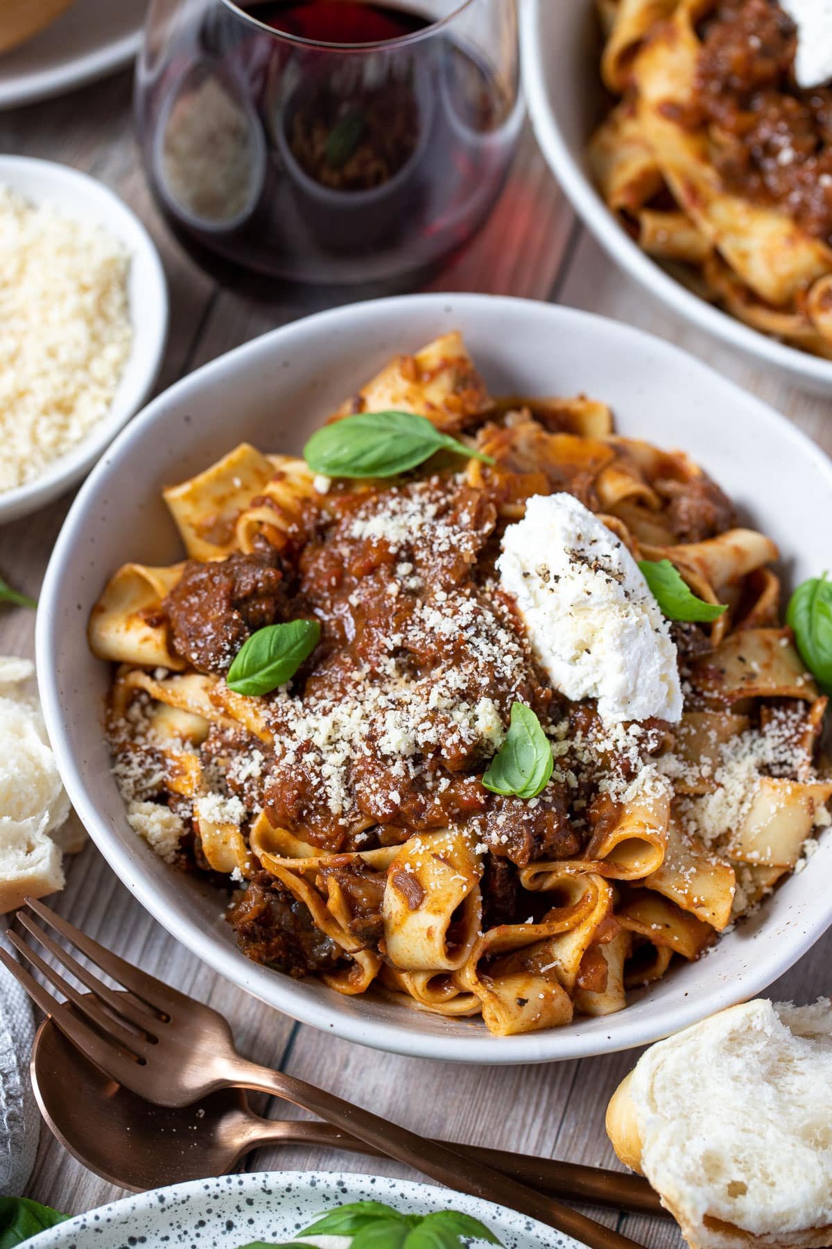 beef cheek ragu with pappardelle pasta in a bowl, topped with ricotta and cheese.