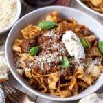 a bowl of beef ragu and pappardelle pasta, topped with cheese and ricotta.