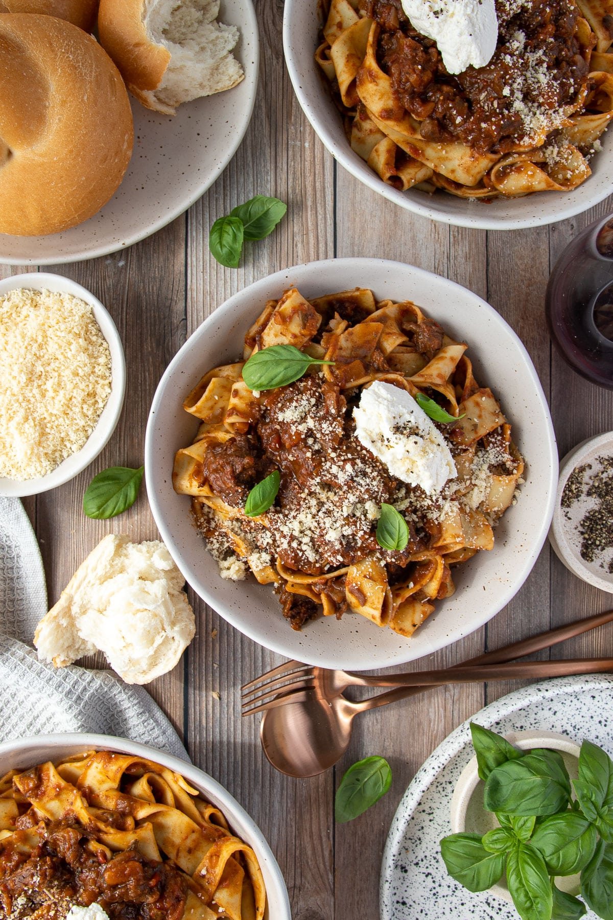 bowls of pappardelle pasta and beef cheek ragu topped with cheese and basil leaves.