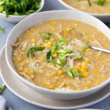 a bowl of soup topped with shredded chicken, pieces of corn and spring onions.