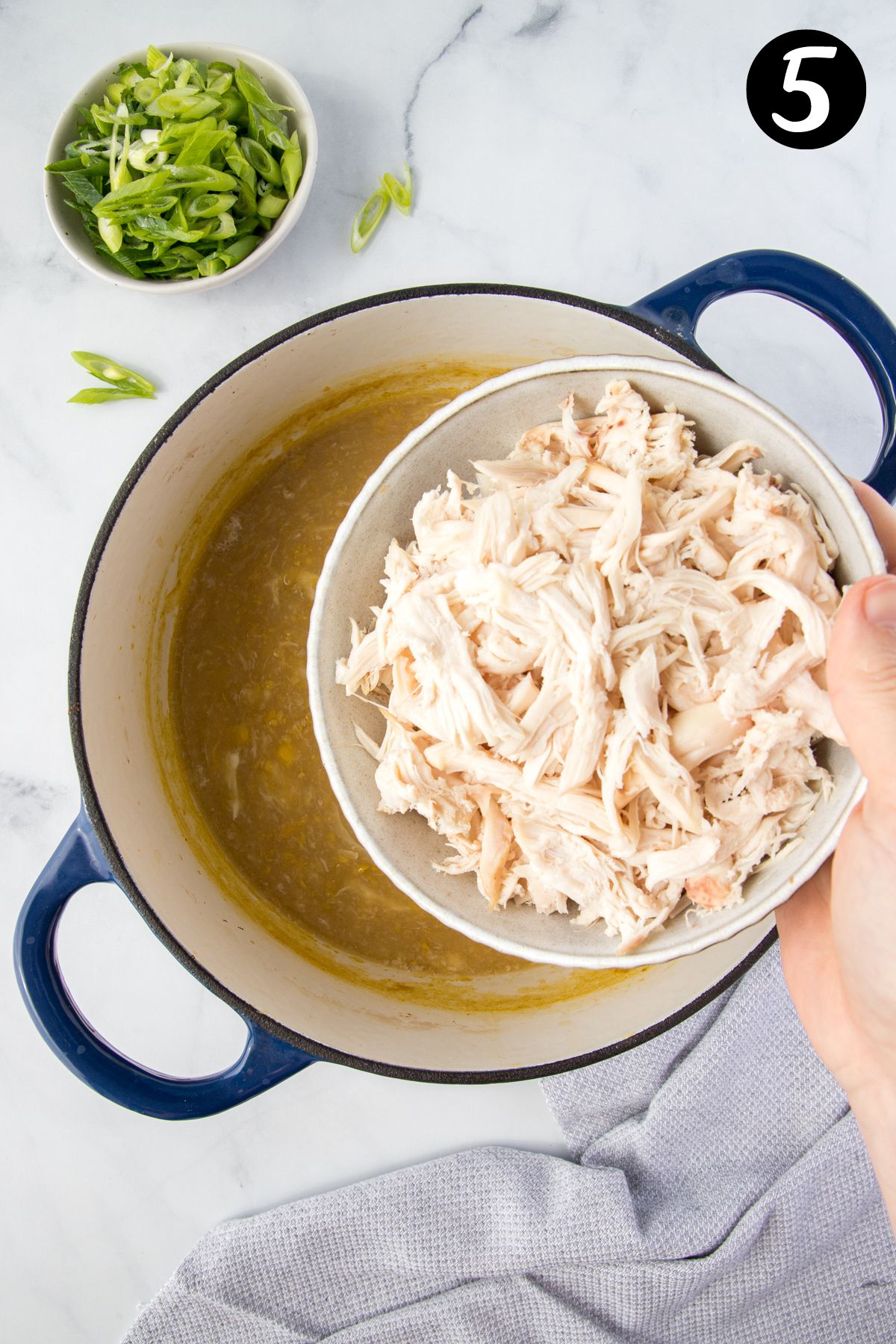 a bowl of shredded chicken being added to a pot of soup.