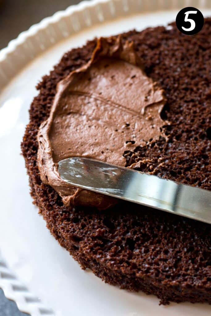 a spatula spreading frosting over a cake on a plate.