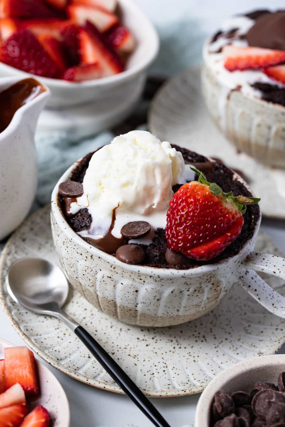 chocolate cake in a mug on a table with ice cream and strawberries.