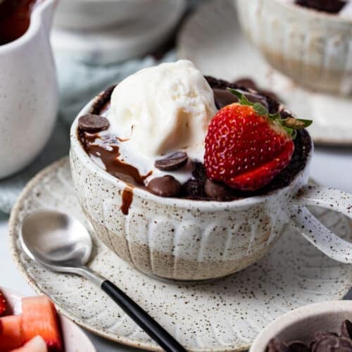 chocolate mug cake on a table, topped with strawberry and ice cream.