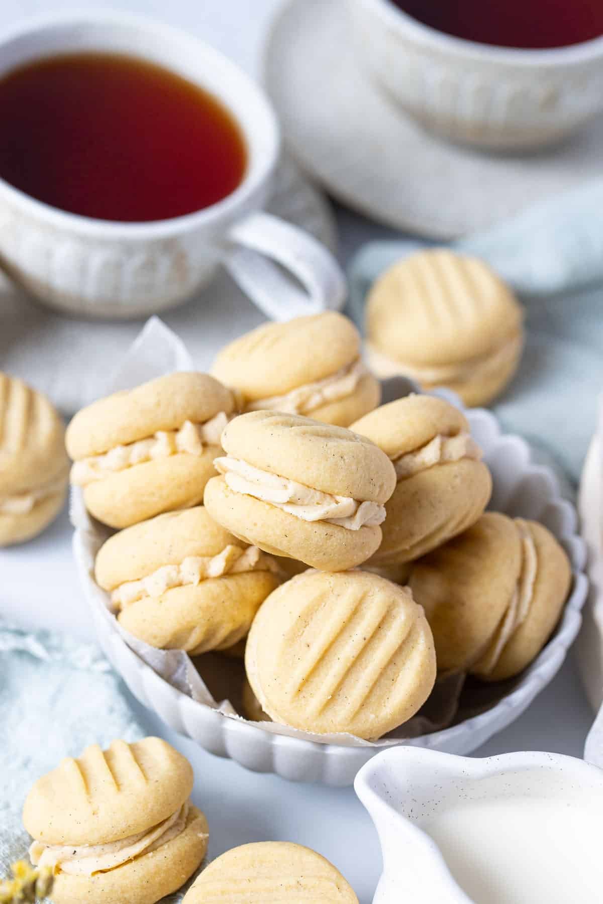 a bowl of melting moments on a table with tea cups.