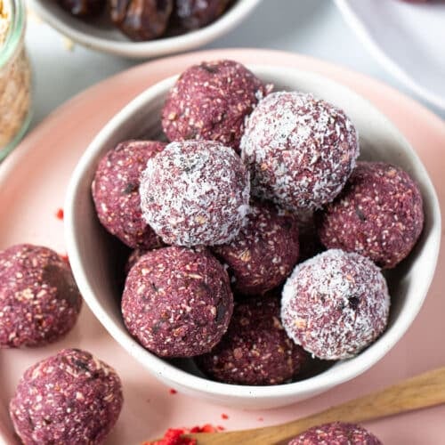 a bowl of purple coloured bliss balls, some are coated in coconut.