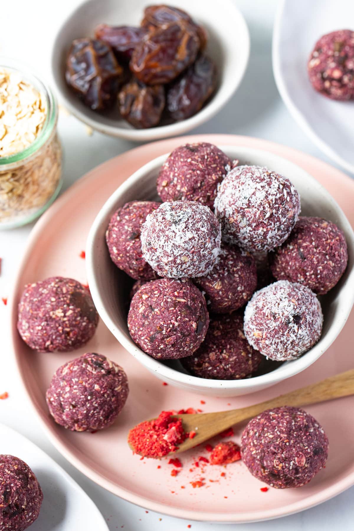 raspberry bliss balls in a bowl with bowls of dates and oats.