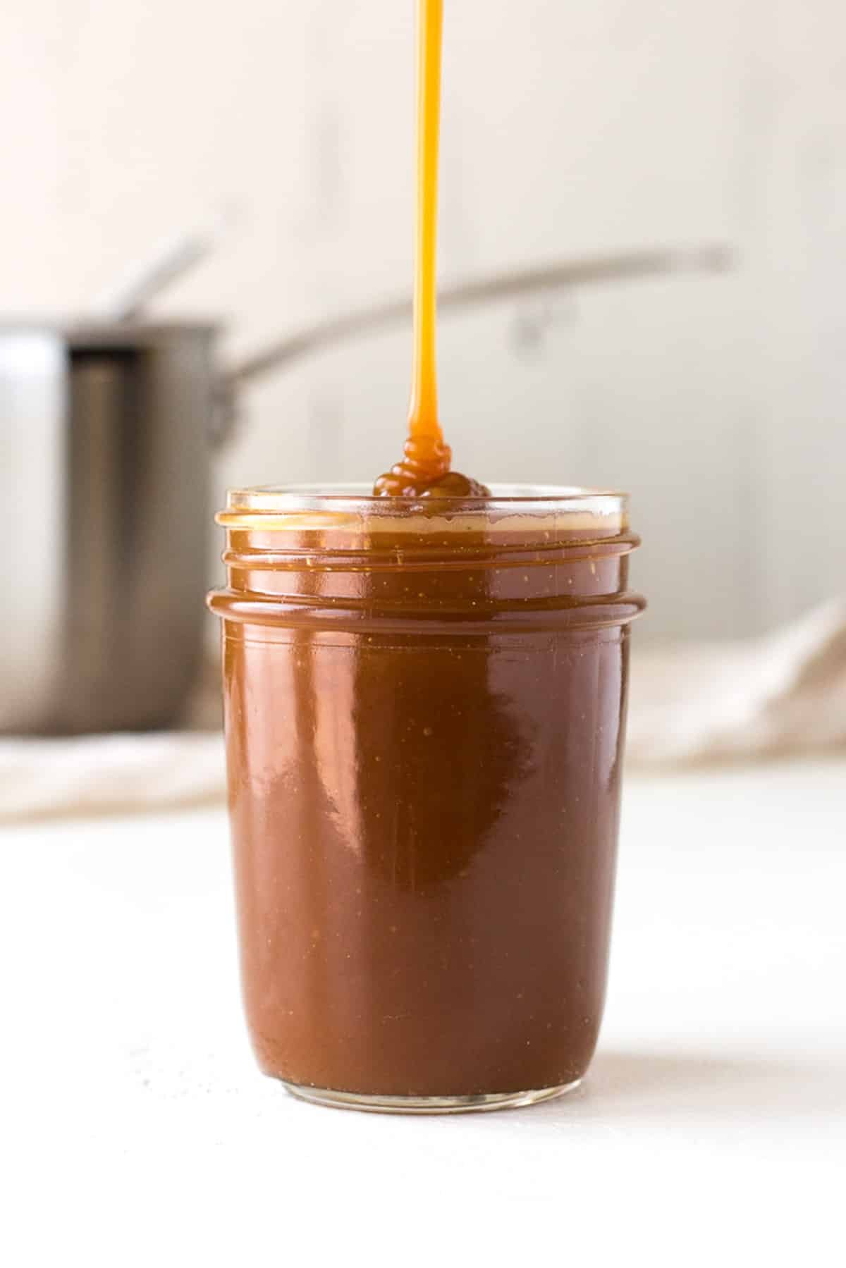 caramel sauce being drizzled into a glass jar.