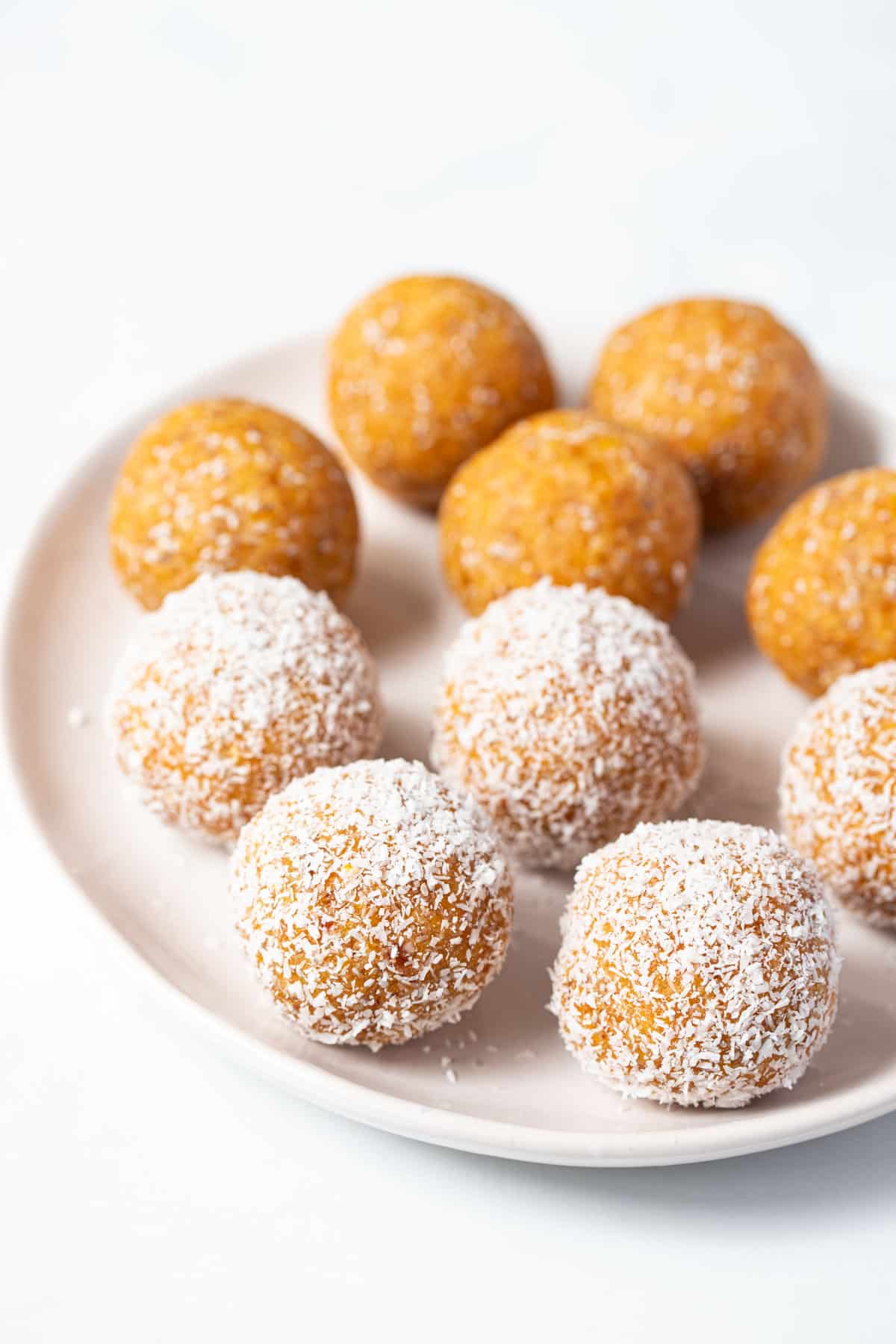 apricot balls rolled in coconut on a white plate.