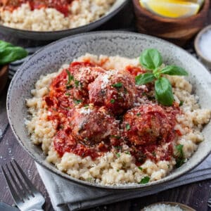 a bowl filled with pearl couscous and topped with meatballs, tomato sauce and basil.