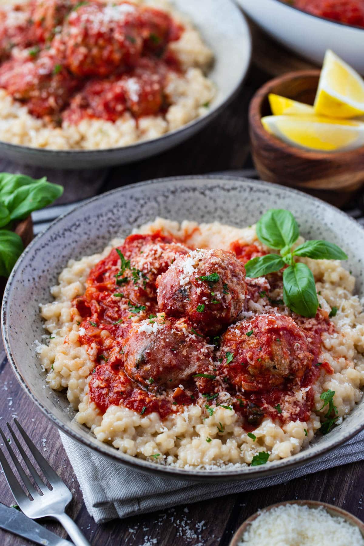 a bowl with pearl couscous topped with meatballs in tomato sauce and basil.