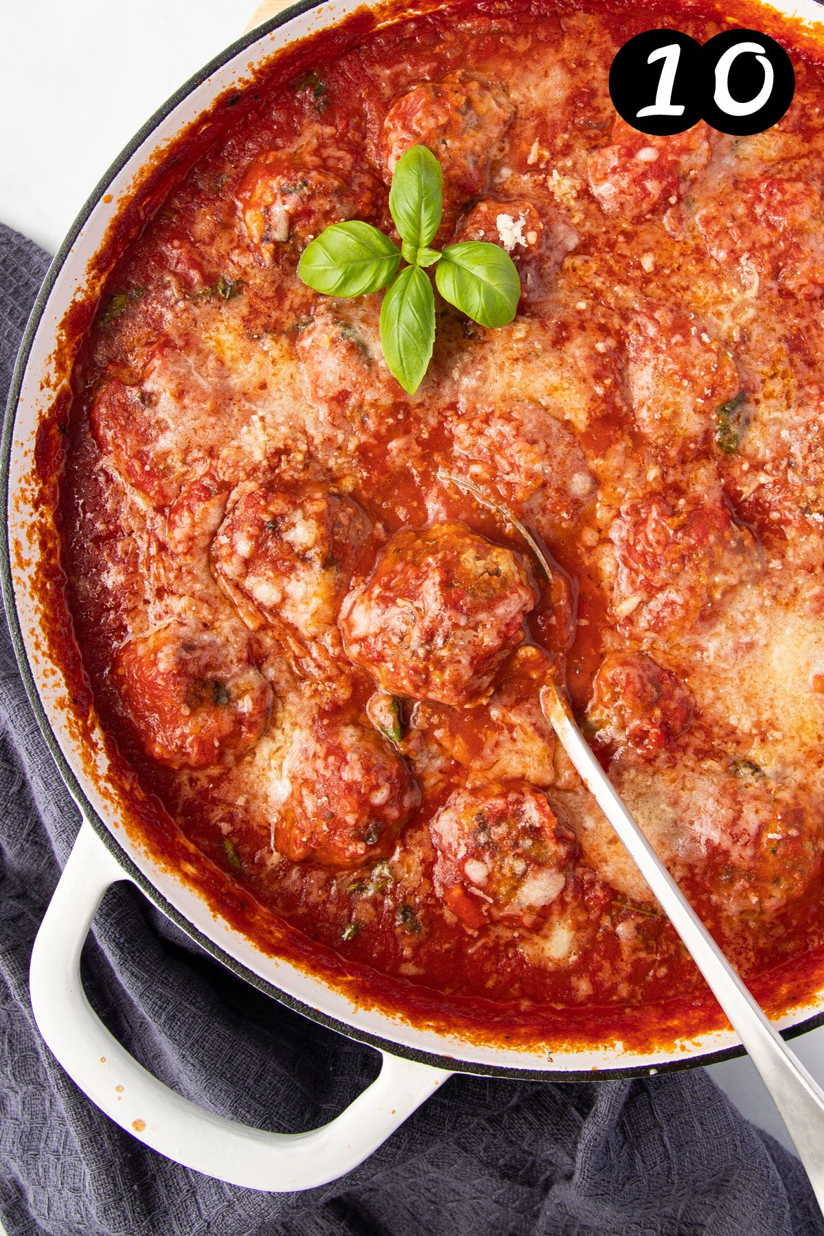 finished meatballs in a pan with tomato sauce, topped with cheese and basil.