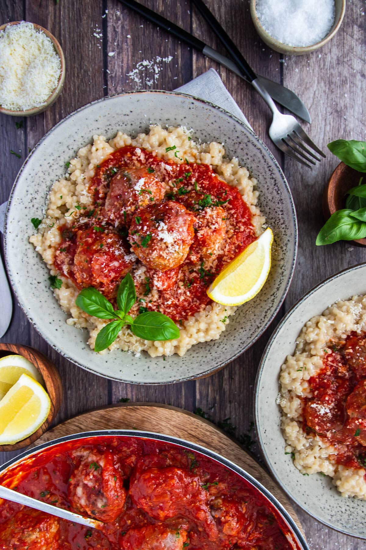 bowls of finished meatballs served in bowls with pearl couscous, lemon and basil.