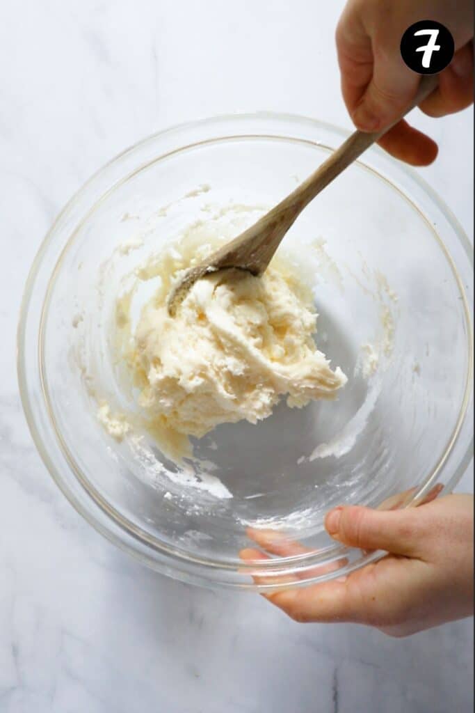 hands stirring lemon icing in a bowl.