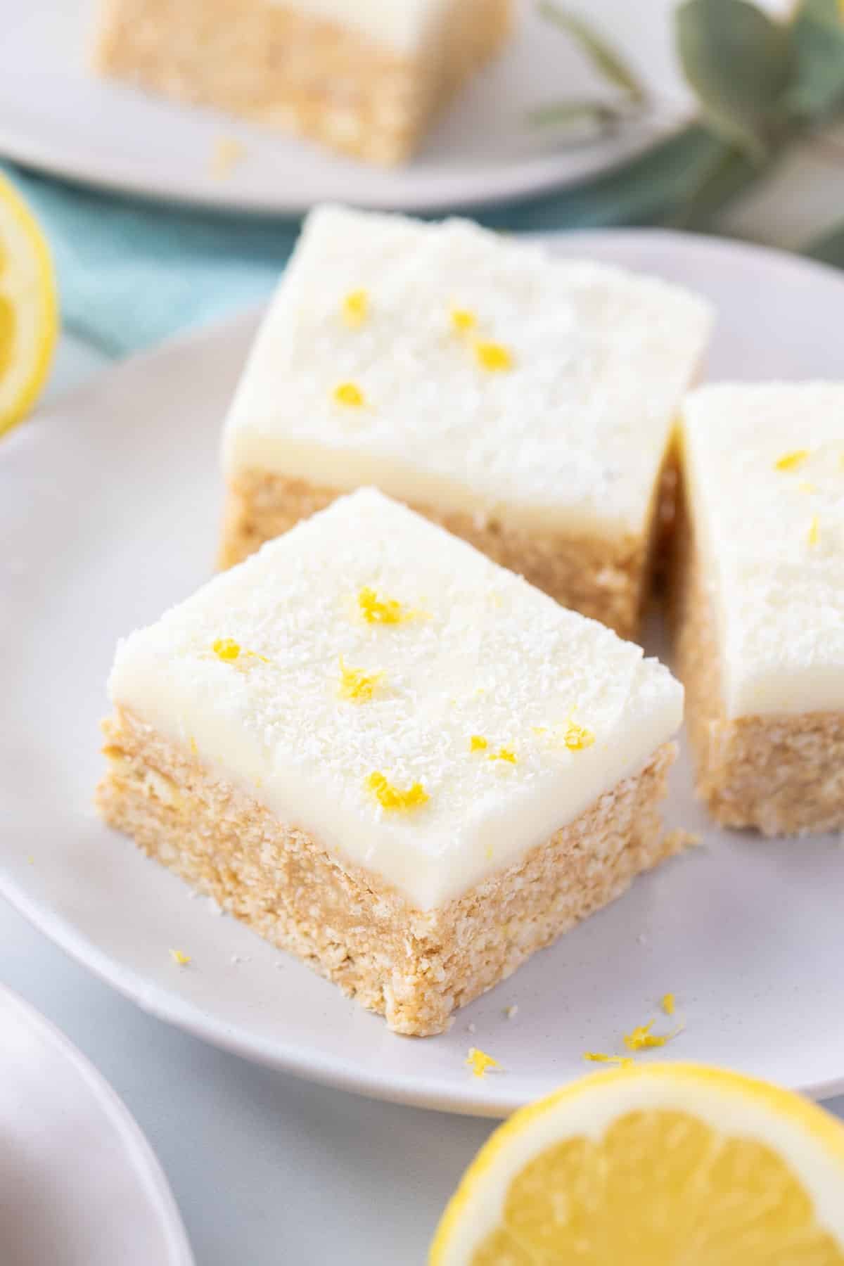 pieces of lemon slice on a white plate, topped with icing, coconut and lemon zest.