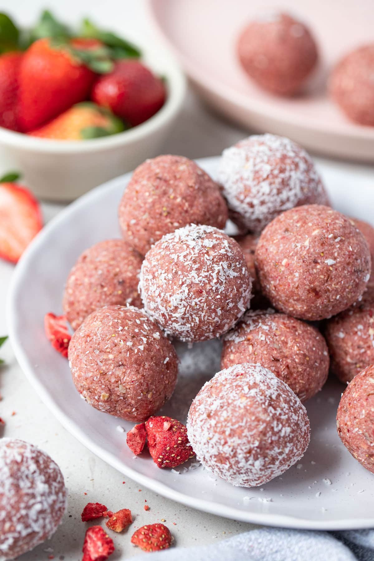 bliss balls coated in coconut stacked on a white plate.