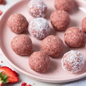 strawberry bliss balls coated in coconut, arranged on a plate.