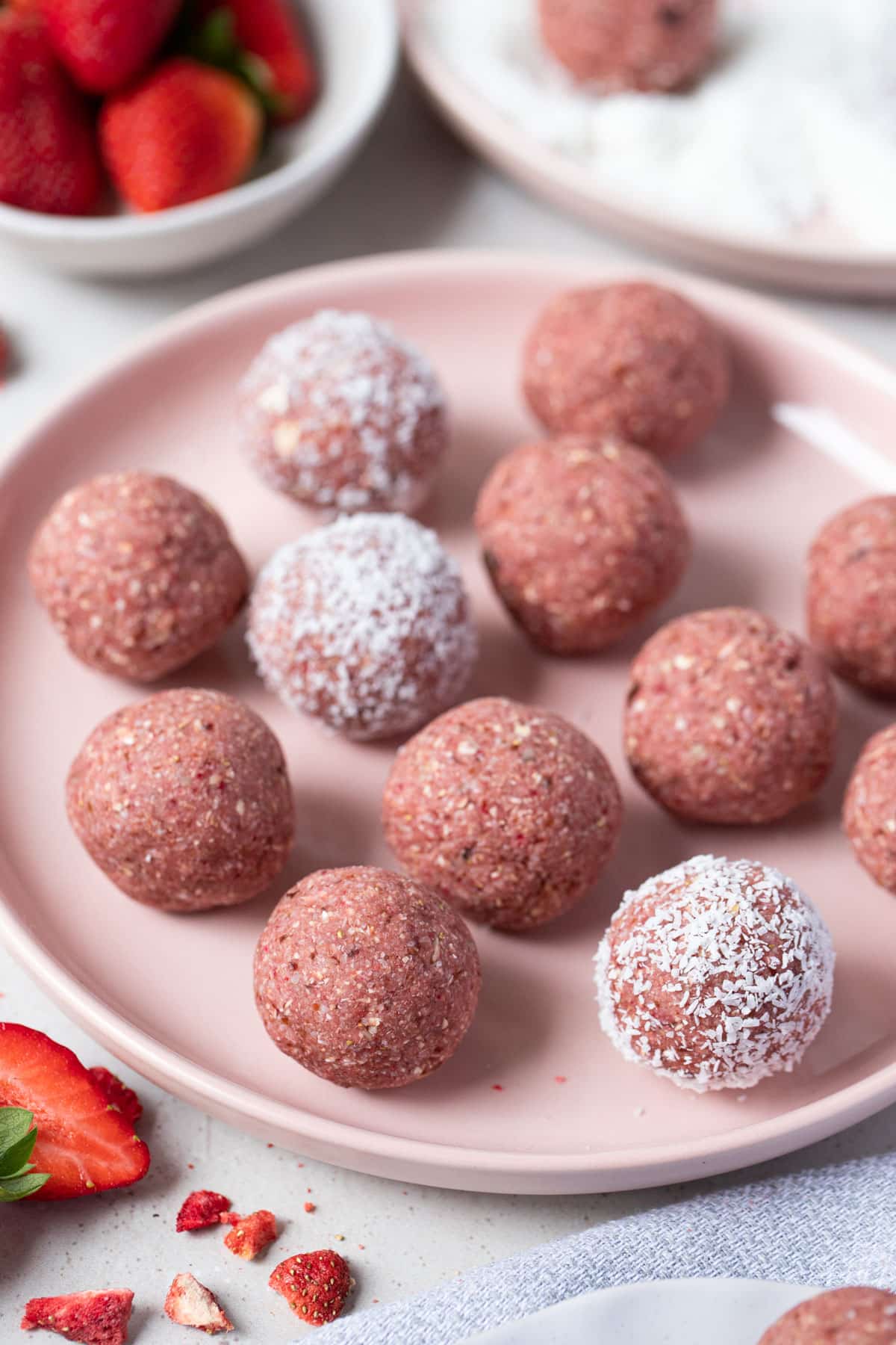 a pink plate with strawberry bliss balls and fresh strawberries.