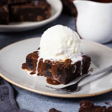 a slice of chocolate brownie on a grey plate, topped with a scoop of ice cream.