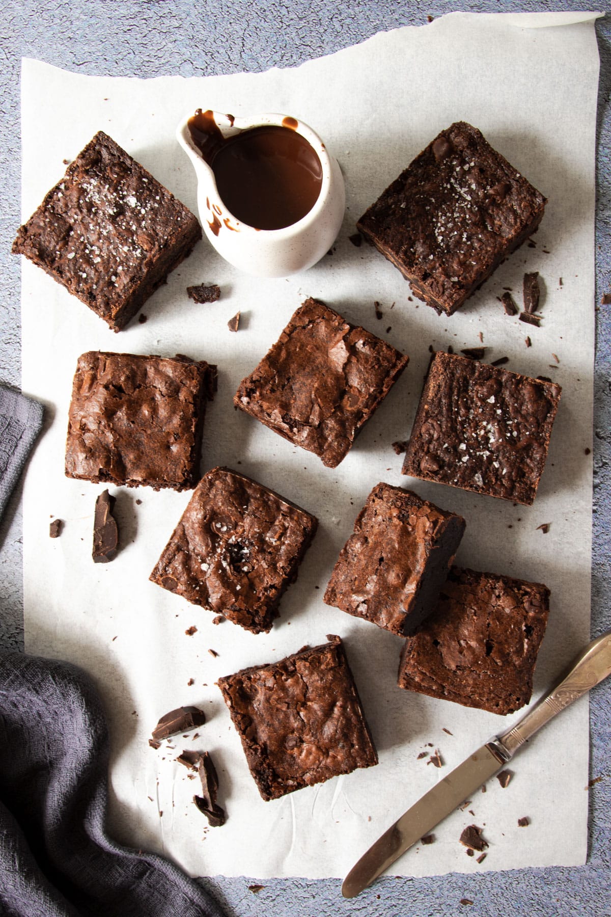 sliced brownies on a sheet of baking paper, with a knife and chocolate sauce.