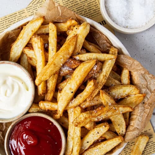 a bowl lined with paper, holding crispy chips and small bowls of dipping sauces.