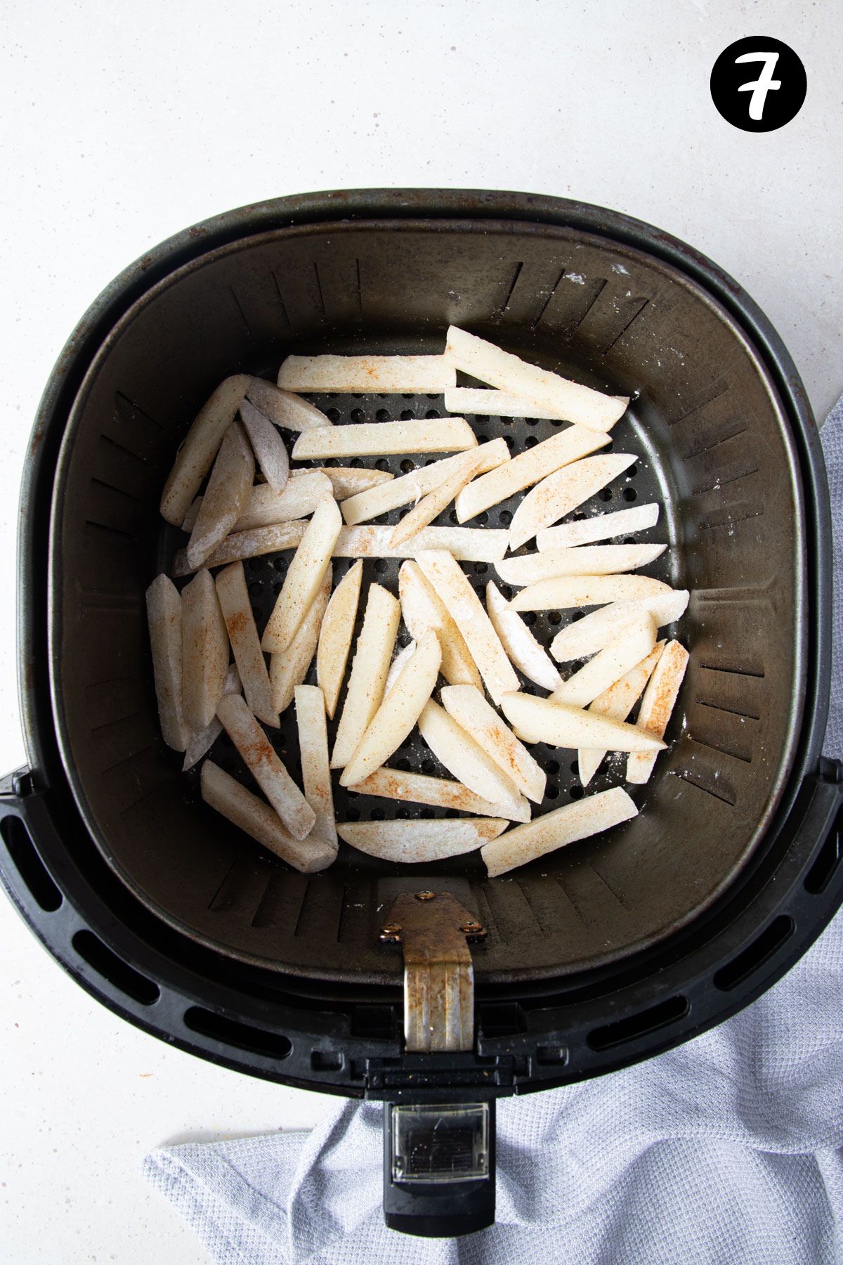 chips in air fryer basket, on a bench.