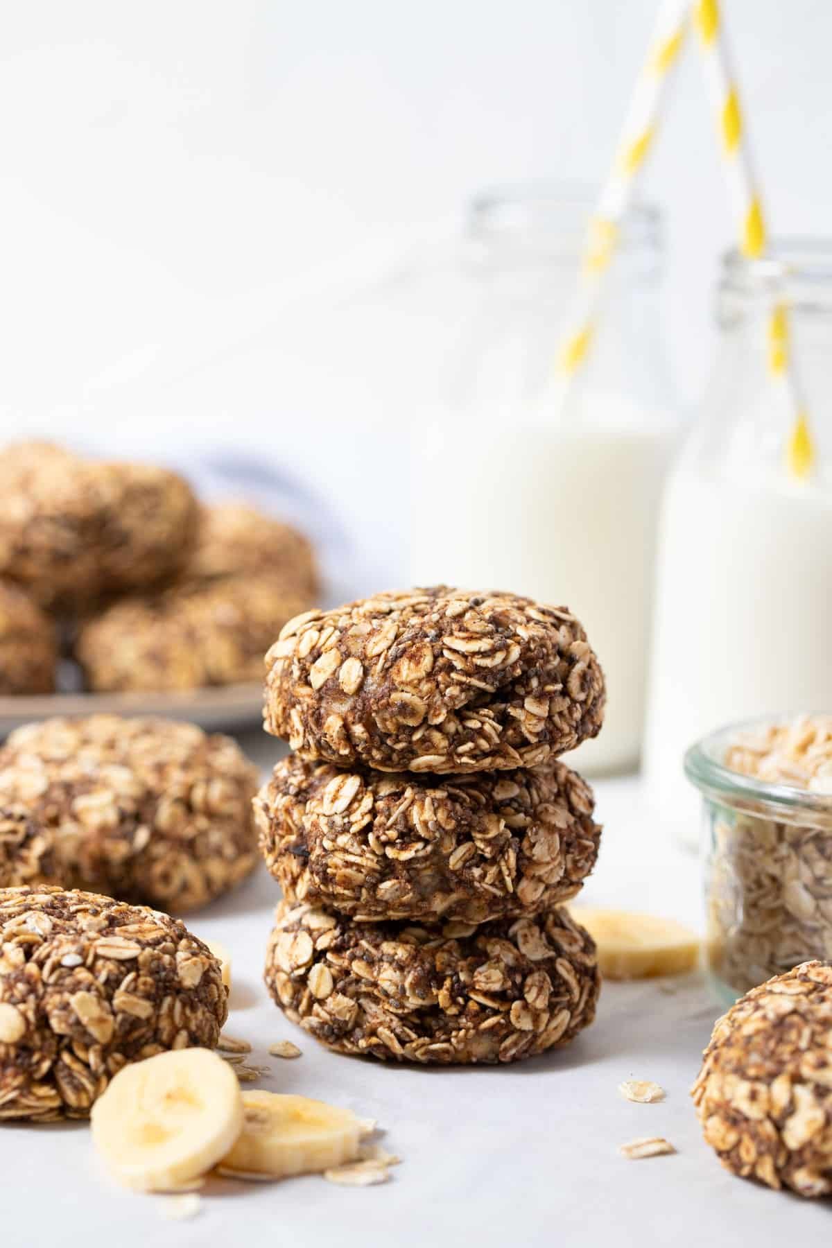 a stack of cookies on a white table with slices of banana and milk.