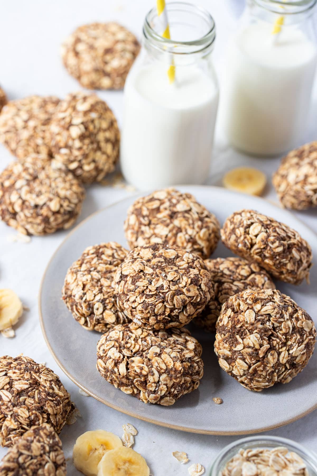 oat cookies on a plate with bottles of milk and slices of banana.