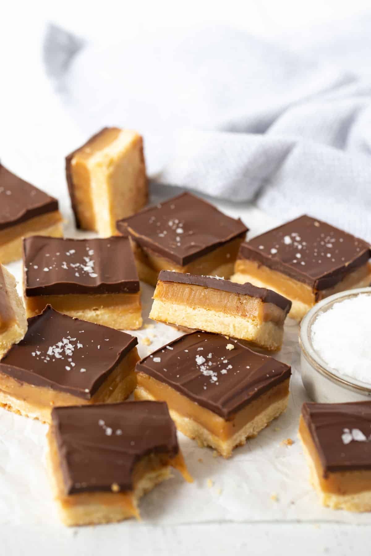 pieces of caramel slice topped with chocolate and salt flakes on a white table.
