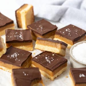 pieces of caramel slice topped with chocolate and salt flakes on a white table.