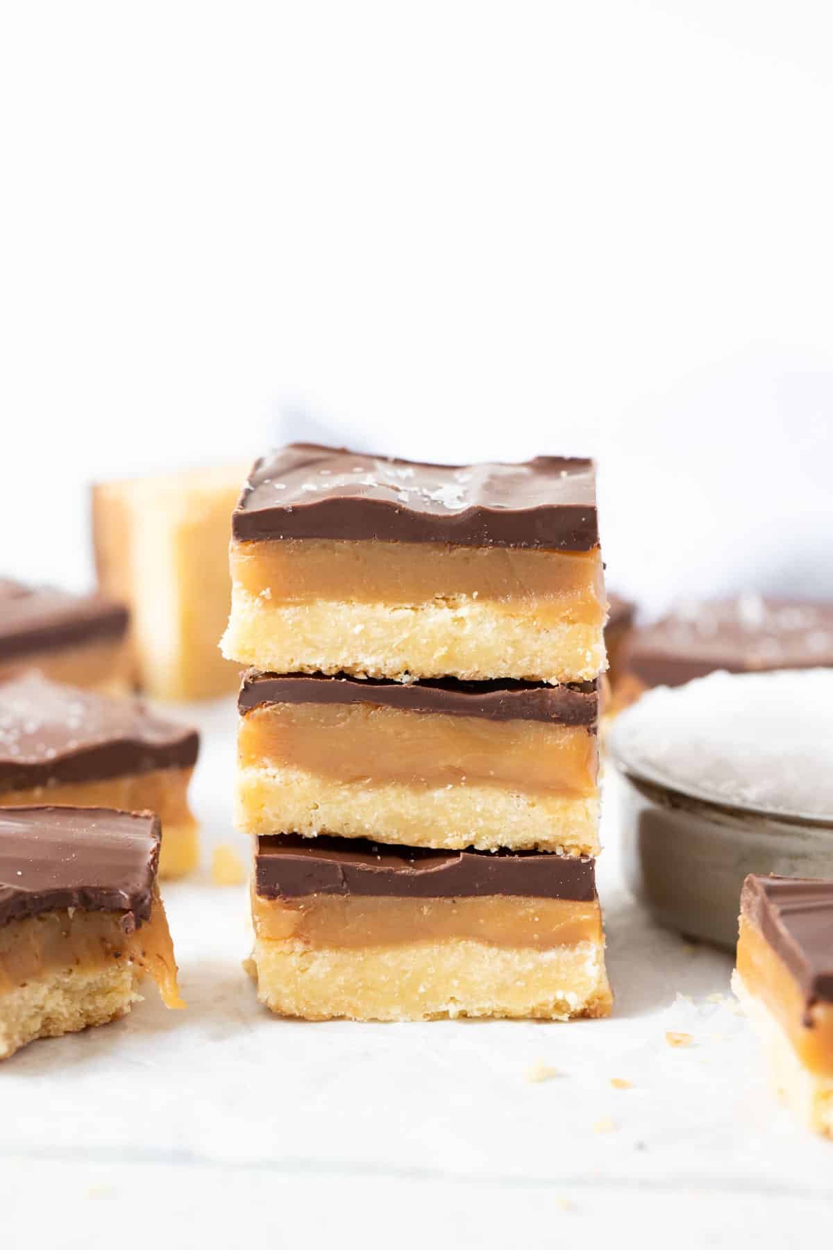 three pieces of caramel slice stacked on a white table.