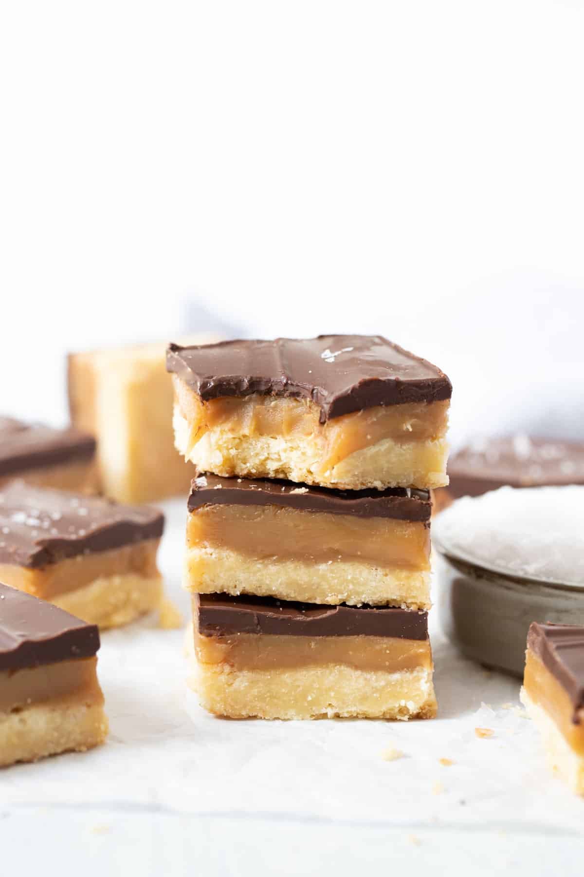 pieces of caramel slice stacked in a pile on a white table.