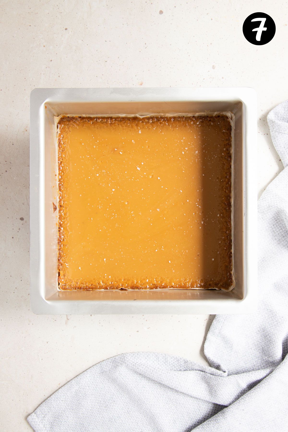 a square baking tin filled with a caramel topping, sprinkled with salt flakes.