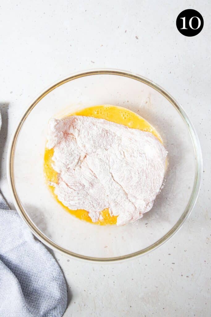 a piece of chicken coated in flour, in a bowl with beaten eggs.