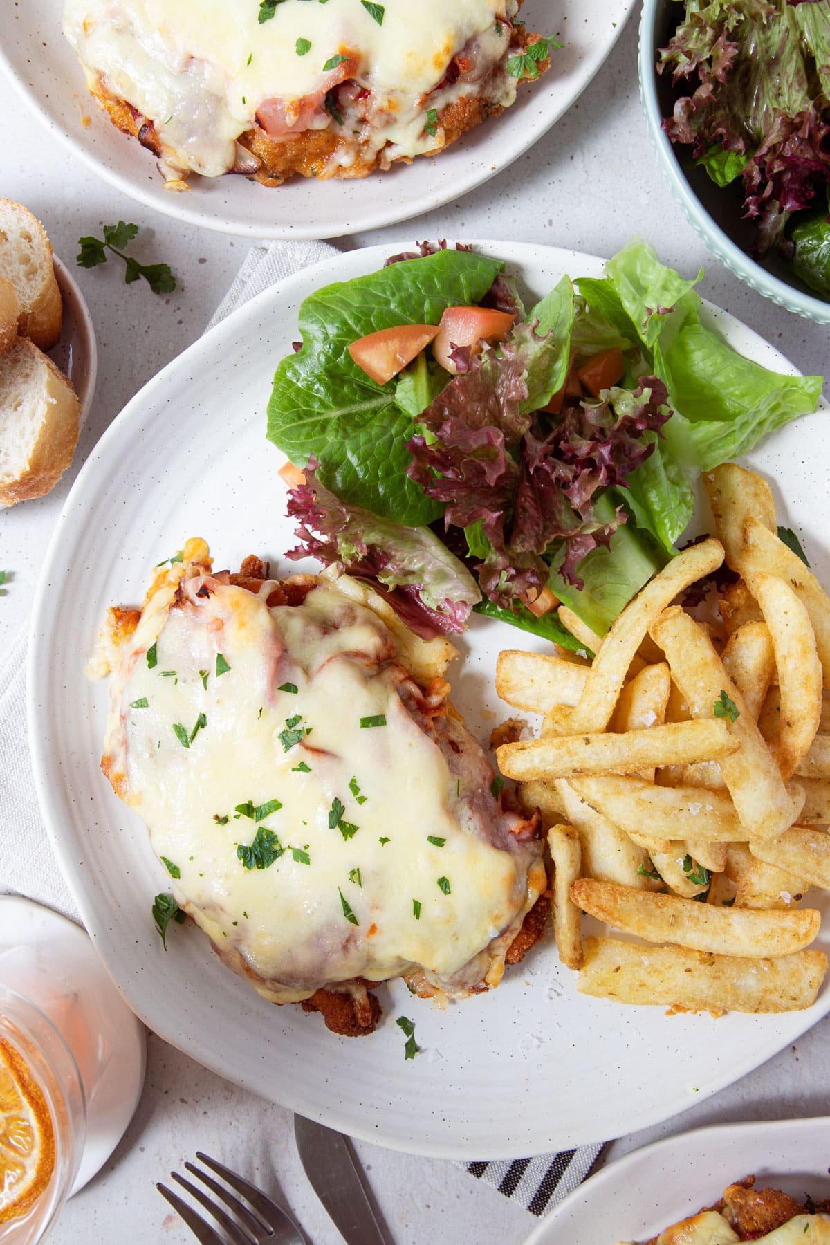 a plate with chicken parmigiana, chips and salad on a dining table.